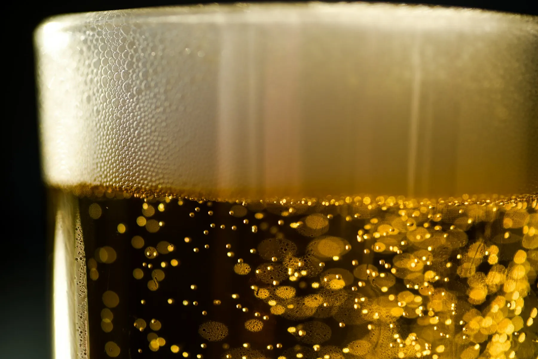 Un bicchiere di birra dorata con una schiuma fitta, ripreso da vicino.