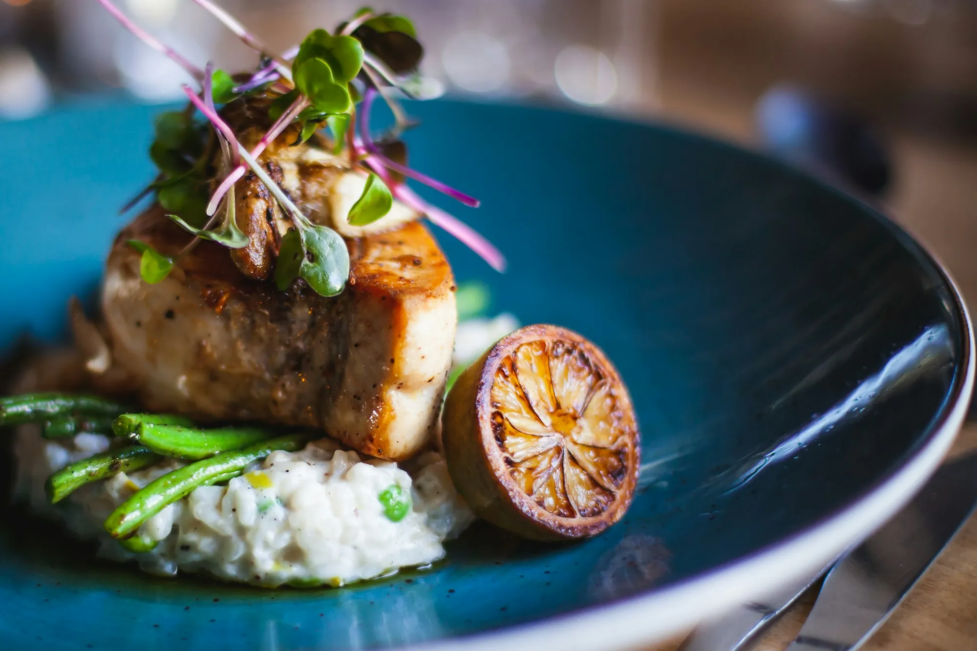Filetto di pesce scottato su risotto e asparagi, in un piatto blu con un limone grigliato