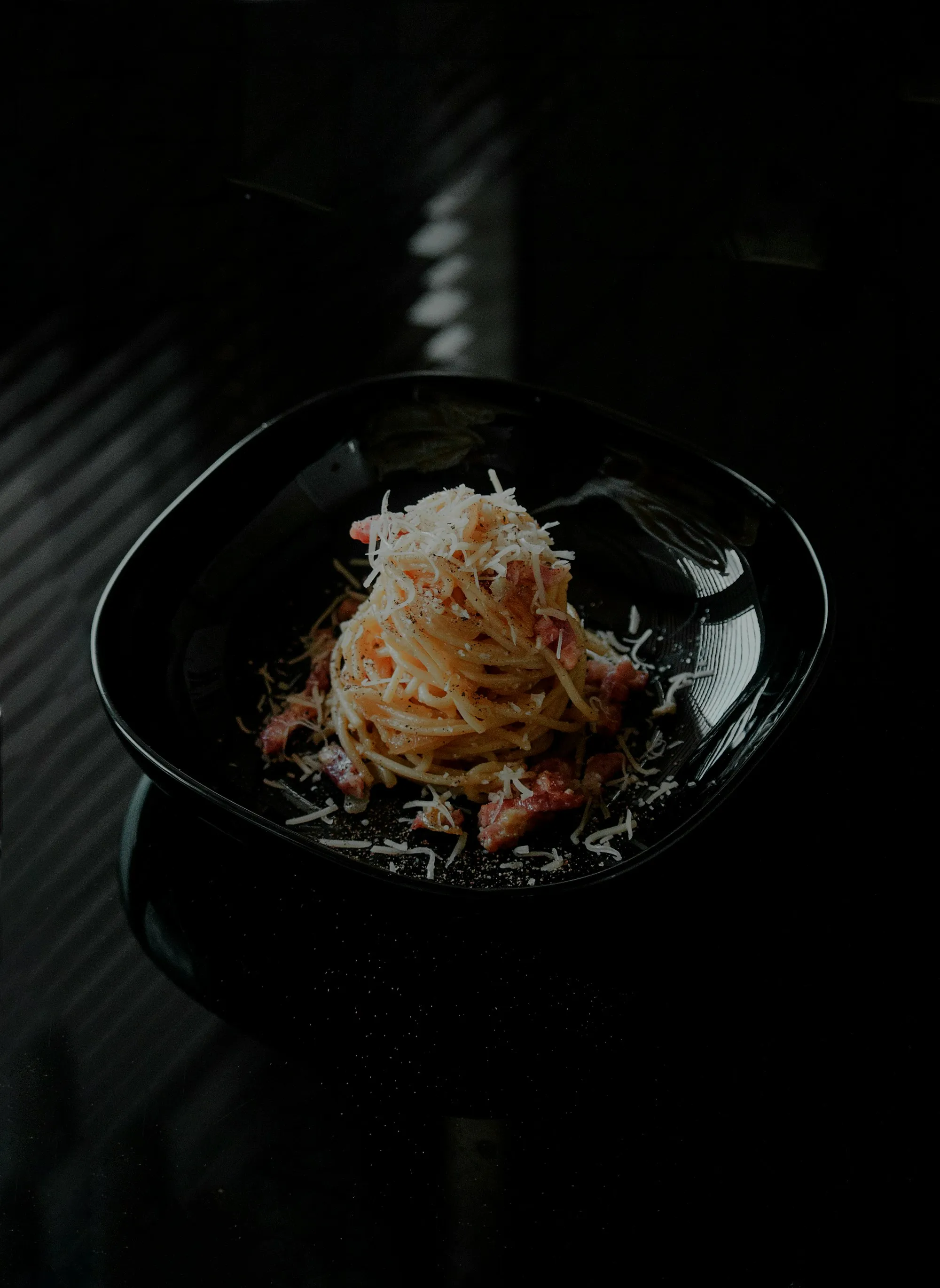 Spaghettone in una ciotola nera su fondo scuro, illuminato da una luce laterale