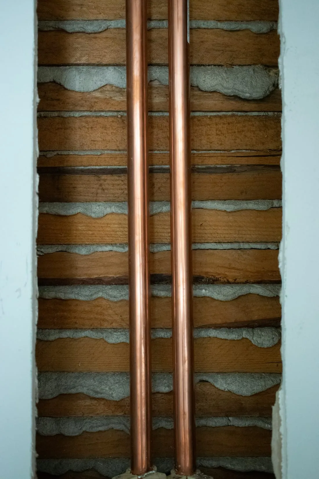 Due tubi di rame appena posati dentro una parete aperta, tra le travi di legno.