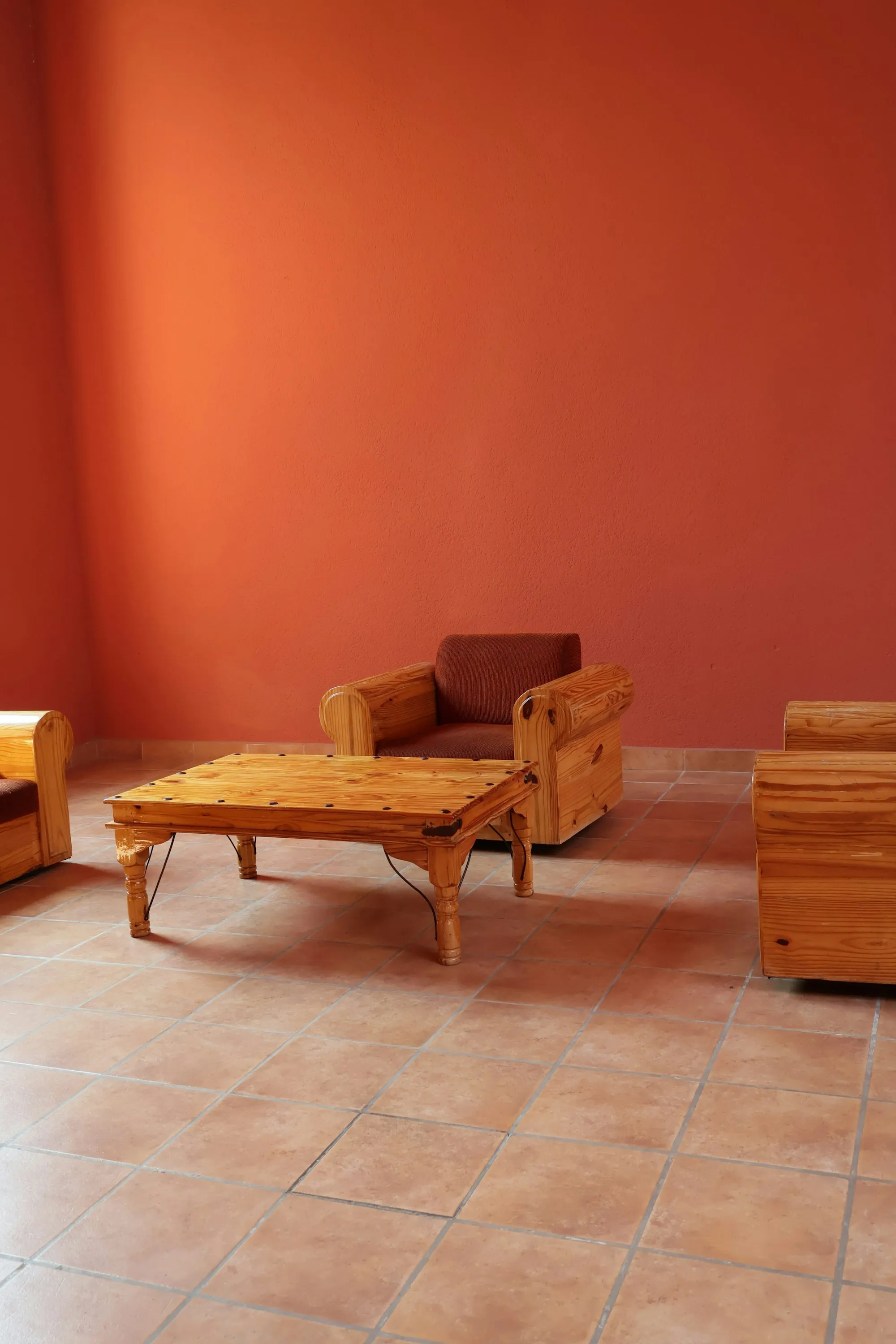 Salón con una pared de cal naranja, suelo de baldosa de barro cocido, un sillón de madera y una mesa baja